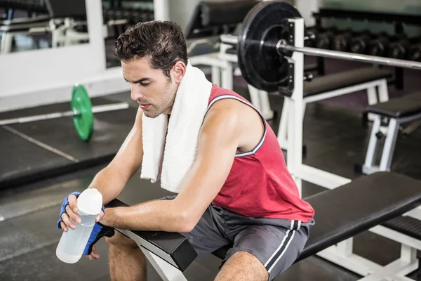 Tired man sitting on bench holding bottle of water — Stock Photo, Image