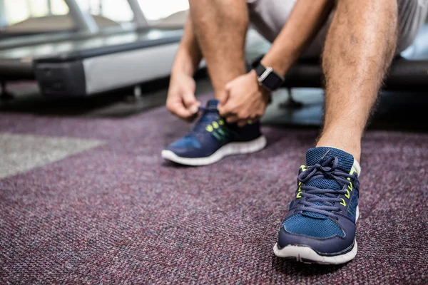 Sección inferior del hombre sentado en la cinta de correr y atar el cordón del zapato —  Fotos de Stock