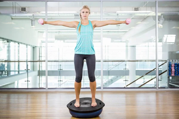 Fit blonde standing on bosu ball and lifting dumbbells — Stock Photo, Image