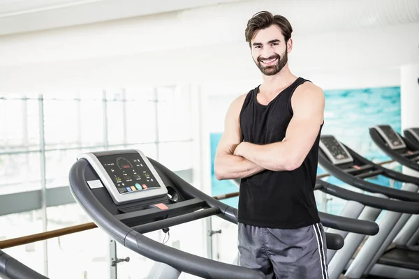 Uomo sorridente in piedi sul tapis roulant con le braccia incrociate — Foto Stock