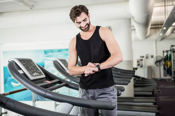 Usmívající se muž na běžeckém pásu při pohledu na smartwatch — Stock fotografie