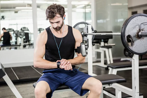 Hombre musculoso sentado en el banco de pesas y usando smartwatch —  Fotos de Stock