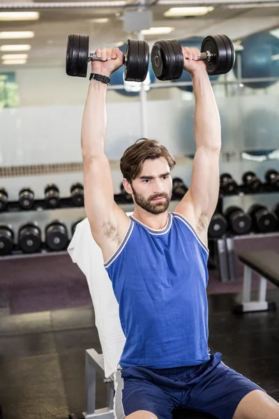 Muscular man lifting dumbbells on bench — Stock Photo, Image