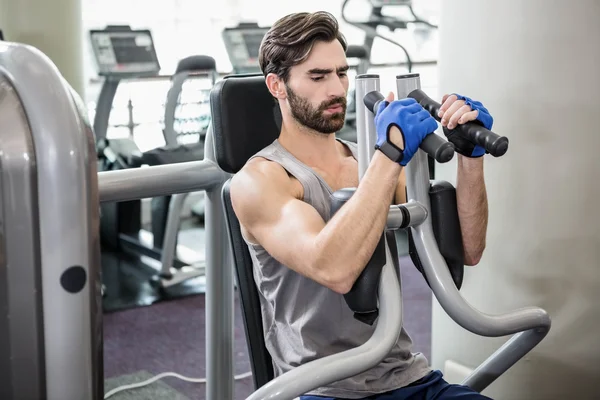 Uomo concentrato che utilizza la macchina pesi per le braccia — Foto Stock