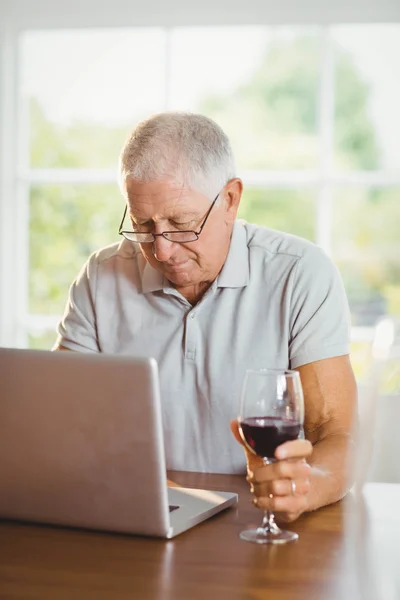 Hombre senior enfocado usando laptop y bebiendo vino —  Fotos de Stock