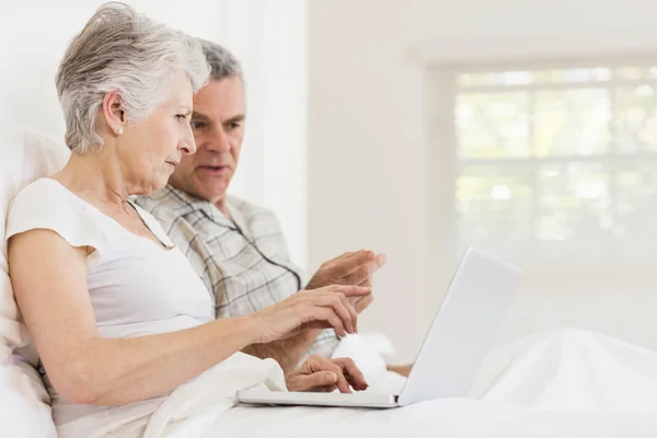 Äldre par med laptop på bed — Stockfoto