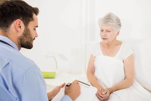 Home nurse listening to elderly woman and writing on clipboard — Stock Photo, Image