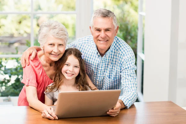 Smiling grandparents and granddaughter using laptop — Stock Photo, Image