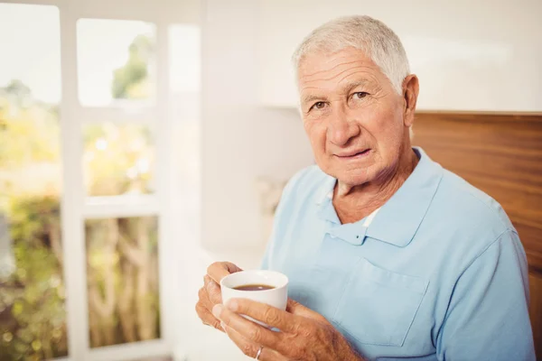 Hombre mayor sosteniendo la taza y mirando a la cámara — Foto de Stock