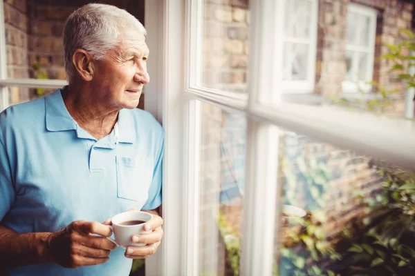 Hombre mayor sosteniendo la taza y mirando por la ventana — Foto de Stock