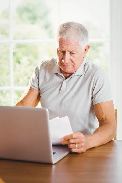 Starszy mężczyzna trzyma arkuszy i korzysta z laptopa — Zdjęcie stockowe
