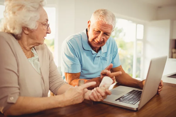 Senior paar met behulp van laptop en pillen te houden — Stockfoto