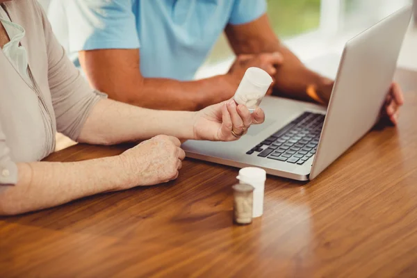 Seniorenpaar benutzt Laptop und hält Pillen in der Hand — Stockfoto