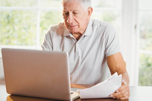 Äldre man innehar dokument och använder bärbar dator — Stockfoto