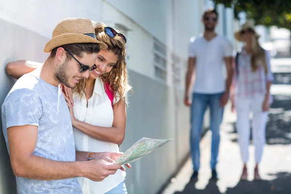 Hip couple checking map and leaning against wall — Stock Photo, Image