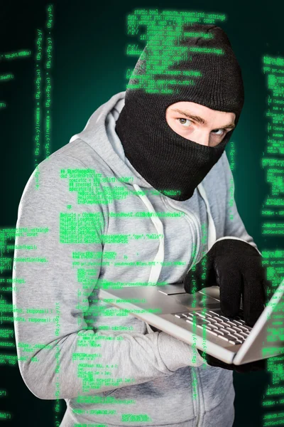 Focused thief with hood typing on laptop — Stock Photo, Image