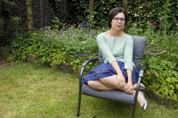 Portrait of trendy girl in glasses sitting on chair in backyard — Stock Photo, Image