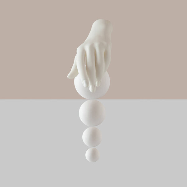 Creative arrangement with artificcial hand and white balls over pastel beige and white  background. Minimal surreal idea concept 