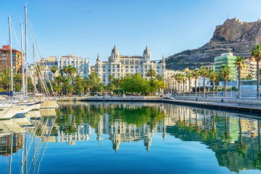 Alicante 'nin yatları, palmiye ağaçları ve Santa Barbara Kalesi Castillo de Santa Barbara Limanı' nın sularına yansıyan manzarası