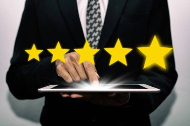 5 yıldız puanı. İş adamı müşteri eli mobil tablete dokunuyor ve iyi derecelendirme, dijital pazarlama, iyi deneyim, pozitif düşünce ve müşteri geri besleme kavramını gözden geçirmek için beş yıldız düğmesi var.