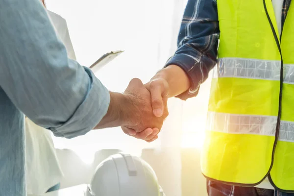 Müteahhit. İnşaat işçileri, inşaat alanındaki toplantı odasındaki çalışma masasındaki proje sözleşmesinden sonra el sıkışıyor. Müteahhit, mühendislik, ortaklık, inşaat konsepti.