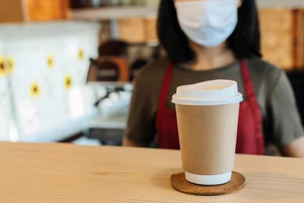 hot black coffee cup on counter with waitress staff wearing protection face on background in coffee shop, food delivery, cafe restaurant, takeaway food, small business owner, food and drink concept