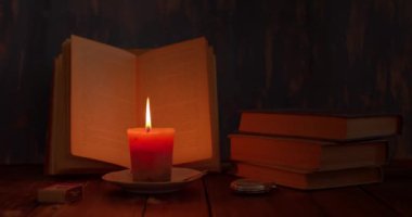 Hayat devam ediyor, masada bir mum yanıyor, açık bir kitap ve yanında bir saat var, retro.