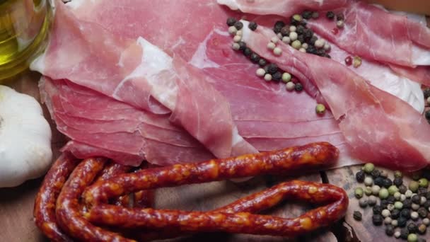 Närbild på tunna skivor prosciutto med torr rå korvar och pepparkorn på trä skärbräda — Stockvideo