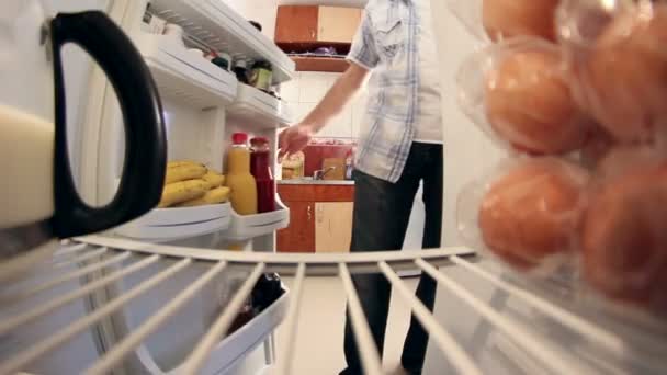 Чоловік дивиться в холодильник, щоб отримати молоко — стокове відео