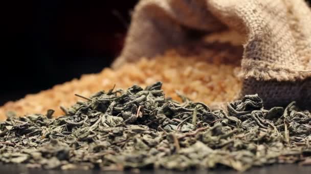 Brauner Zucker in einem feuchten Sack und einem Haufen getrockneter grüner Teeblätter, rotierend — Stockvideo