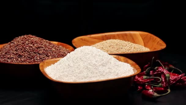 Arroz vermelho, grãos de painço, pérolas de tapioca em pequenas tigelas e uma pilha de pimenta seca, rotativa — Vídeo de Stock