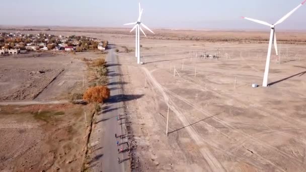 Cyclists ride along road with a view of windmills. — Stock Video