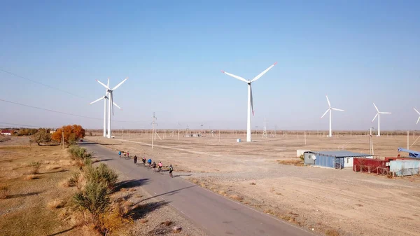 Bisikletçiler yol boyunca yel değirmenlerinin manzarasıyla gezerler..