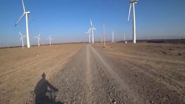 Los ciclistas viajan por carretera con vistas a los molinos de viento. — Vídeos de Stock