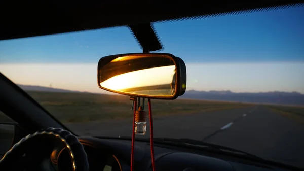汽车的后视镜和黎明 橘红色的黎明笼罩着山丘 汽车在高速行驶 草地和草地清晰可见 这辆车的黑色 方向盘 引擎盖 — 图库照片