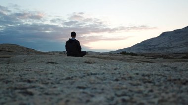 Bir adam şafak vakti dağlarda meditasyon yapar..