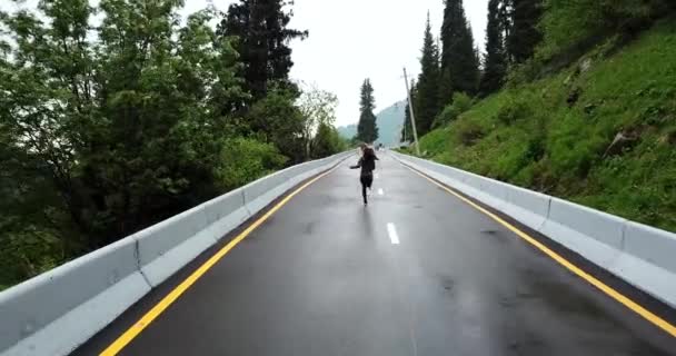 Ein Mädchen läuft auf nassem Asphalt in den Bergen. — Stockvideo