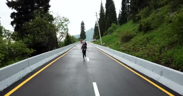 Una chica corre sobre asfalto mojado en las montañas. — Vídeos de Stock