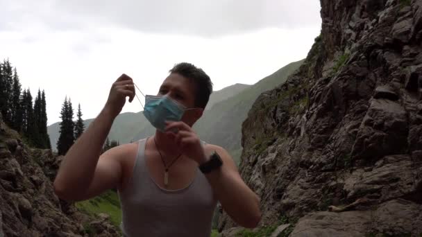 Парень в горах снимает свою медицинскую маску. — стоковое видео