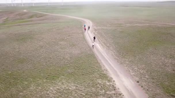 Μια ομάδα ποδηλατών κινείται κατά μήκος των ανεμόμυλων. — Αρχείο Βίντεο