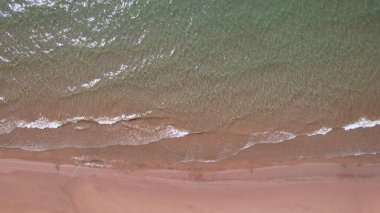 Deniz sarı kuma dalgalarla dokunuyor. Temiz bir sahil ve zümrüt sularındaki bir dronun üst görüntüsü. Güneşin ışınları suya yansıyor. Açık mavi gökyüzü. Rahatlamak için bir yer. Kapchagai