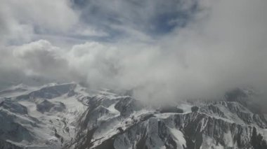 Hava perspektifi, büyüleyici karlı dağ zirvelerini kısmen bulutlarla gizliyor, doğanın ihtişamını gözler önüne seriyor, kamera gelişmekte olan manzarayı yakalamak için kap ve zumluyor.