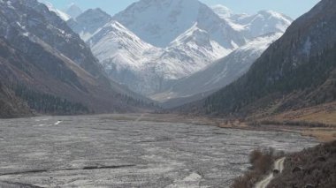 Görkemli dağ manzaraları, yüksek tepelerle çevrili geniş bir nehir yatağını gözler önüne seriyor, kamera çarpıcı derinliği ve doğal güzelliği gözler önüne seriyor, dokuları ve renkleri vurguluyor.