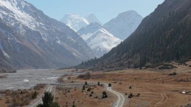 Manzaralı dağ manzarasında bir araç bir vadi boyunca dolambaçlı bir yolda ilerliyor, görkemli tepeler ve yemyeşil alanlarla çevrili, doğanın güzelliğini gözler önüne seriyor, kamera sorunsuzca hareket ediyor.