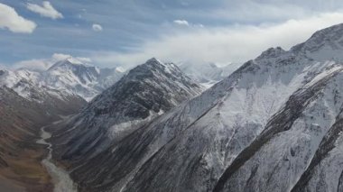 Karla kaplı tepeleri ve aşağıda kıvrımlı bir nehri olan görkemli dağ sırası, nefes kesen manzarayı ve manzaranın doğal güzelliğini gözler önüne seren pürüzsüz bir kamera tavasıyla çekiliyor.