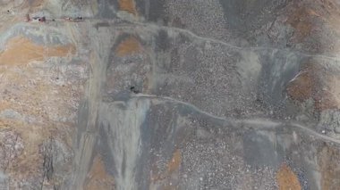 Hava görüntüsü engebeli arazisi ve kazı alanı olan bir maden sahası yakalıyor, kamera yakınlaştıkça manzaranın karmaşık detaylarını gösteriyor, hareket halindeki dokuları ve makineleri ortaya çıkarıyor