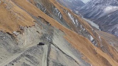 Bir araç sarp ve engebeli bir dağ yolundan geçer, dramatik manzarayı gözler önüne serer. Kamera aracı pürüzsüz bir hava hareketiyle takip ediyor, geniş manzara ve dokuları yakalıyor.