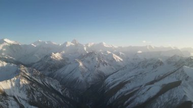 Görkemli dağ silsilesi, açık mavi gökyüzünün altında kar kaplı zirveler ve vadileri sergiliyor. Kamera giderek yaklaşarak manzaranın karmaşık detaylarını gözler önüne seriyor.
