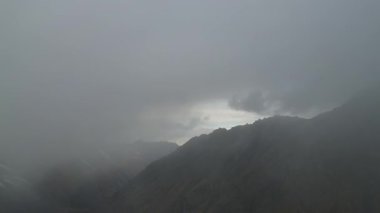 Dağ manzarası sisle kaplanarak, kamera sahnenin diğer tarafına geçerken aşamalı olarak açığa çıkan gizli zirveleri gösteriyor, atmosferde bir gizem ve derinlik hissi yaratıyor.