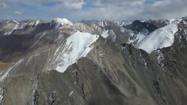 Karla kaplı tepeler ve kayalık arazi içeren görkemli dağ manzarası, kamera nefes kesici manzarada pürüzsüz bir şekilde dönüyor, doğal çevrenin enginliğini ve güzelliğini gösteriyor.